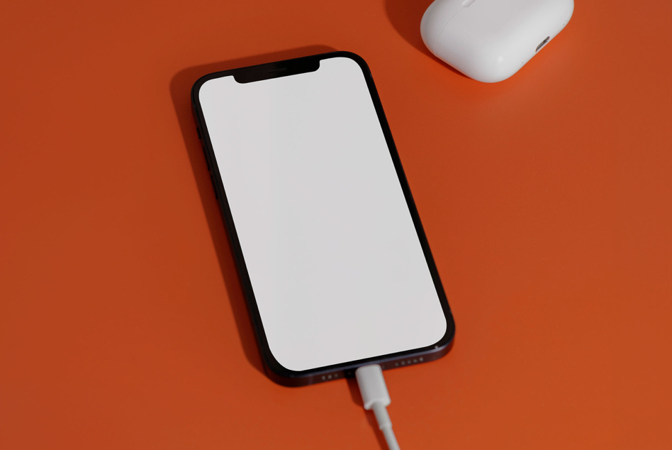 Charged iPhone next to white wireless earbuds case on bright orange backdrop