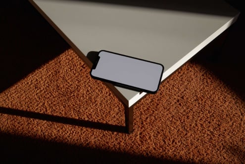Minimal mockup of smartphone on table edge casting shadow on textured carpet; ideal for tech presentations branding or digital design projects.