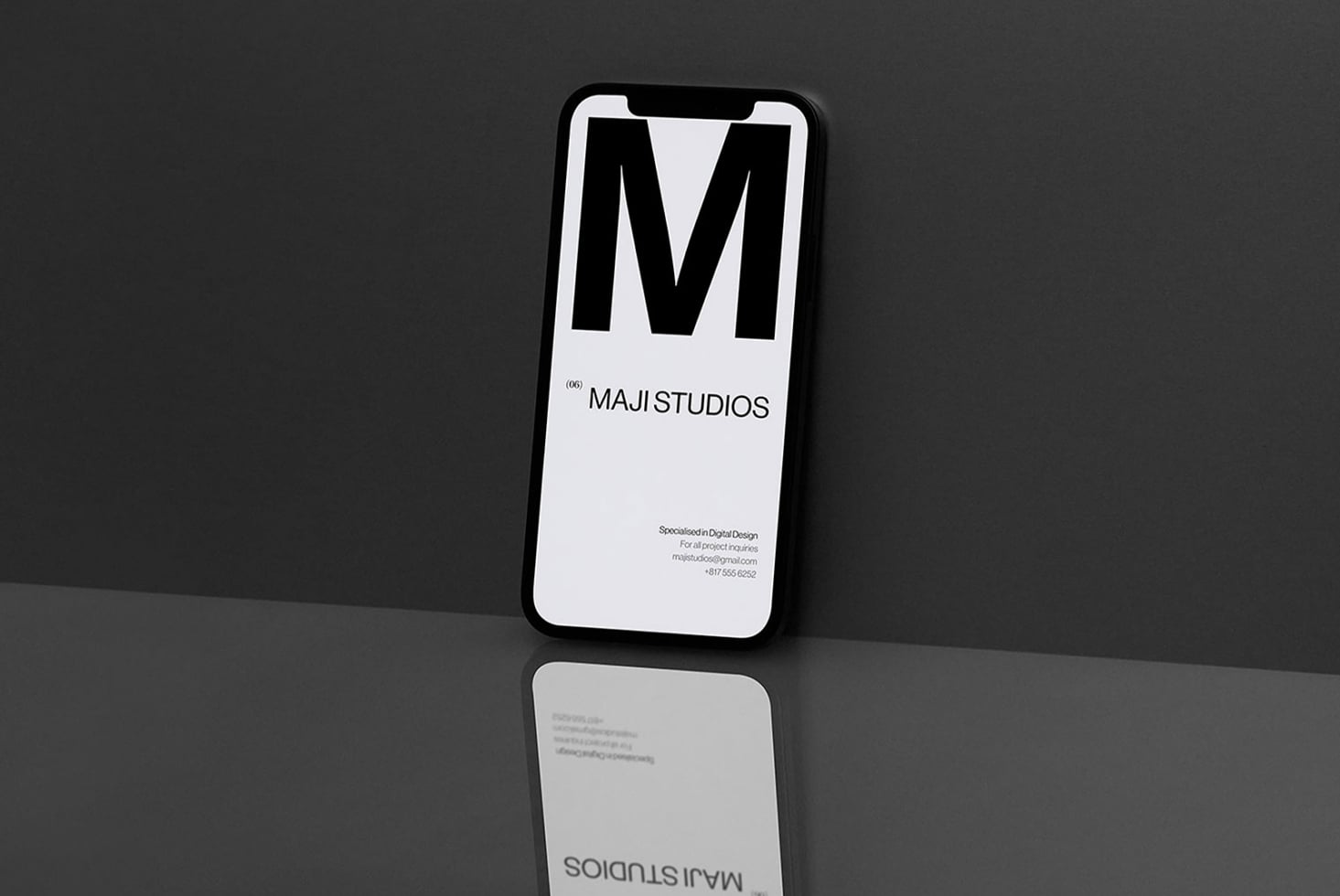 Black iPhone displaying Maji Studios logo in white on light background with contact info