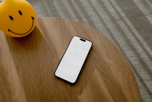 Smartphone mockup on wooden table with smiling yellow ball. Perfect for design presentations. Keywords: mockup, smartphone, design, template, table