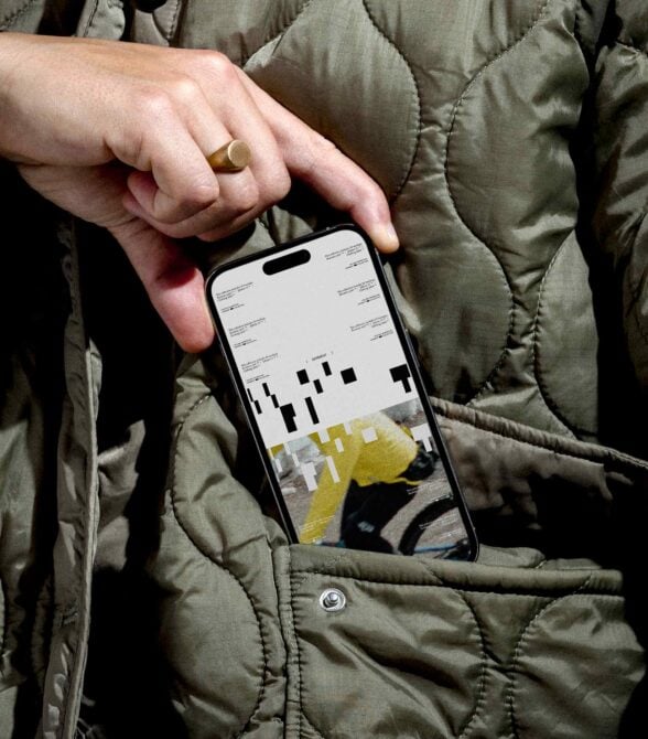 Hand holding phone with yellow design mockup wearing quilted olive jacket