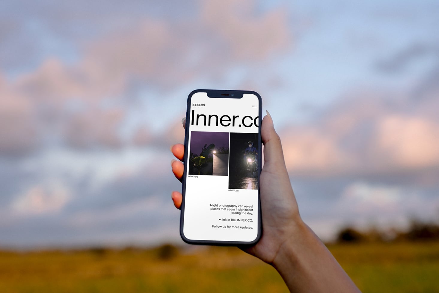 Hand holding phone showing Inner.co website with night photography images on screen