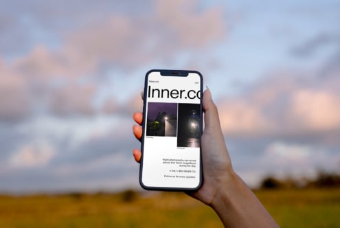 Hand holding smartphone displaying website against blurred sky background. Ideal for mockup templates showcasing mobile responsive web design.