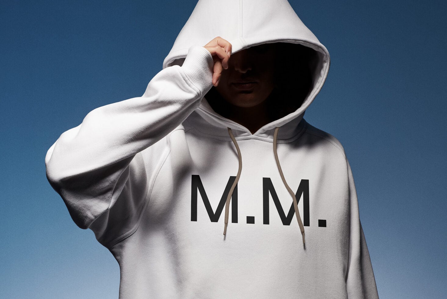 Person in cream hoodie adjusting hood with tan drawstrings visible