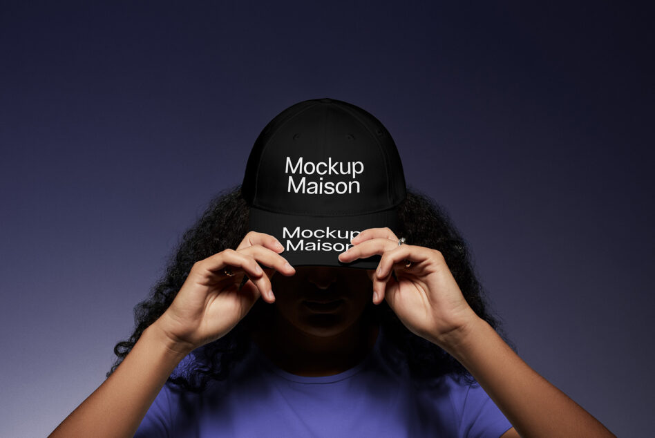 Person holding black baseball cap up to face on deep purple gradient background