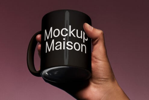 Hand holding a black mug mockup with Mockup Maison text front on a dark background for branding design templates digital assets designers marketplace