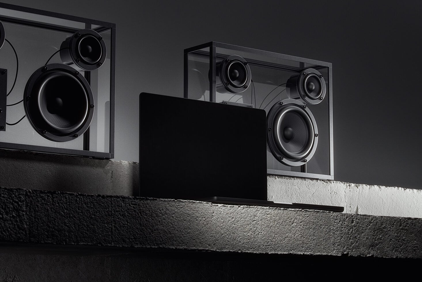 Three dark framed speakers mounted on textured wall with blank black monitor display below