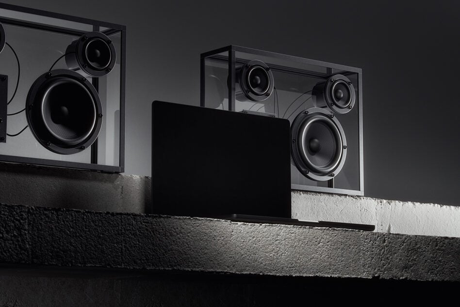 Three dark framed speakers mounted on textured wall with blank black monitor display below