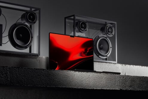 Laptop mockup with vibrant red abstract screen on concrete surface flanked by modern speakers perfect for graphic designers showcasing digital assets
