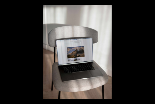 Laptop mockup on a gray chair with sunlight; ideal for showcasing website designs; minimalist home office setting; digital asset for designers.