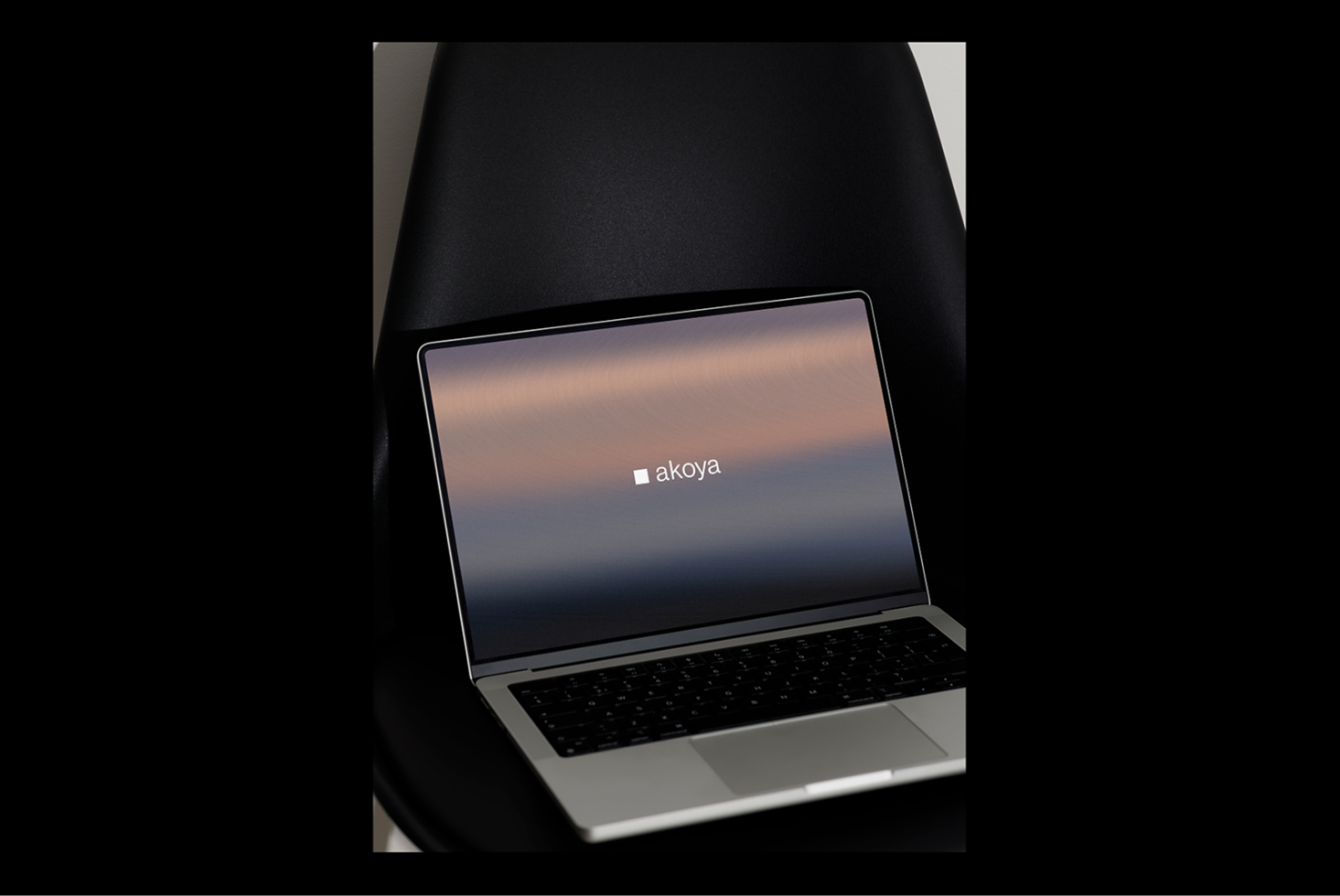Laptop mockup on black chair with Akoya logo and gradient screen background ideal for graphic design templates digital assets designers SEO friendly