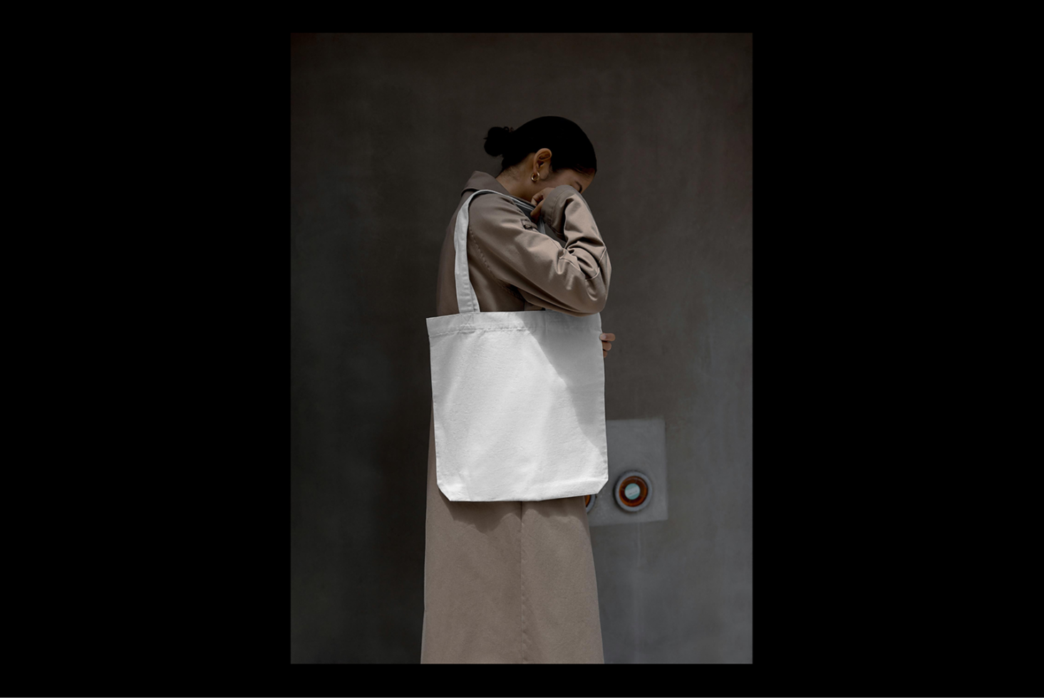Tote bag mockup featuring a person in a neutral-toned coat against a minimalist background ideal for designers branding commercial use digital assets