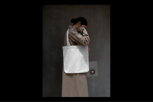 Tote bag mockup featuring a person in a neutral-toned coat against a minimalist background ideal for designers branding commercial use digital assets