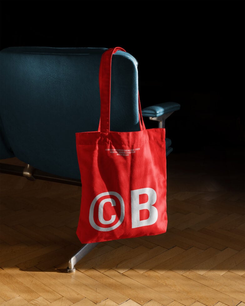 Red tote bag mockup with bold white letters hanging on a blue chair. Ideal for branding designs. Keywords: tote bag mockup, branding, graphic design.