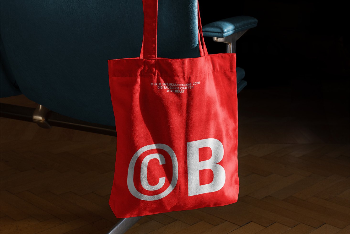 Red tote bag on a blue chair with bold C B logo design. Ideal for branding mockups and designer presentations. Modern design accessory asset.