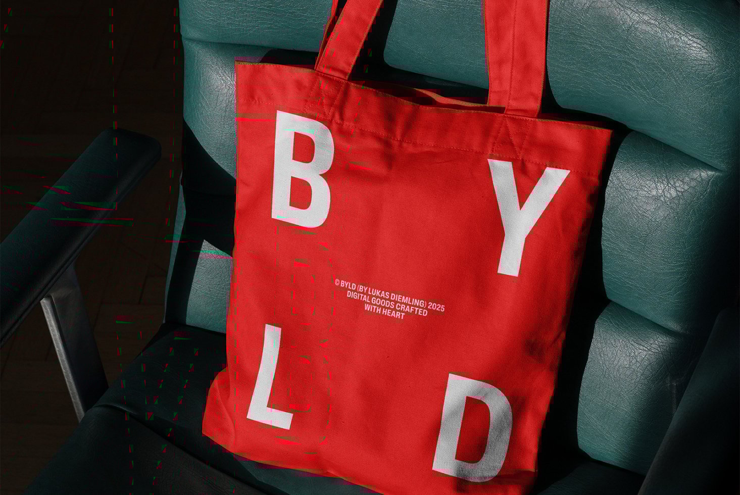 Red tote bag with bold white letters BYLD on green chair. Ideal for branding mockup. Design for creatives, showcasing typography and layout skills.