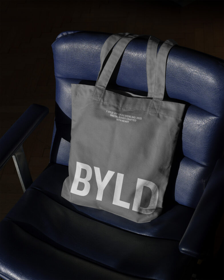 Grey tote bag mockup with bold BYLD logo on a dark blue chair perfect for branding presentations or digital design showcases for designers.