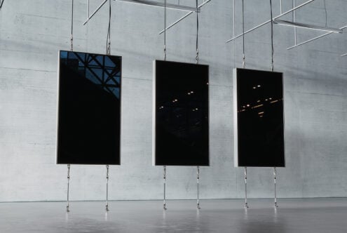 Three modern black display panels suspended with cables in a minimalist, industrial space. Ideal for digital advertising mockups or interior design templates.