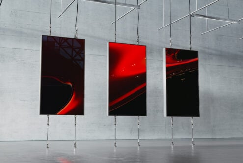 Three modern digital art frames with abstract red and black designs hang in an industrial space. Ideal for showcasing in graphic design mockups.