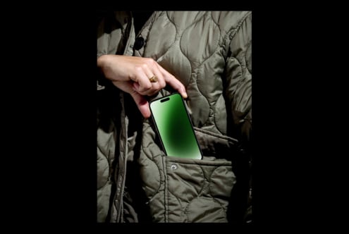 Hand inserting smartphone into a quilted jacket pocket. Green screen for mockup. Ideal for digital assets designers. Fashion tech concept image.