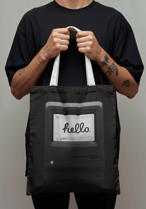 Person wearing black tee holding black tote bag with retro computer screen graphic
