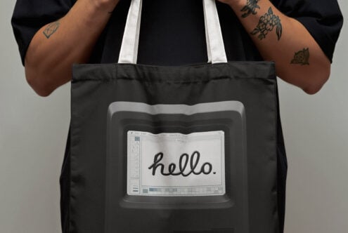 Tote bag with vintage computer screen design featuring the word hello held by tattooed hands. Ideal for graphic design and template use.