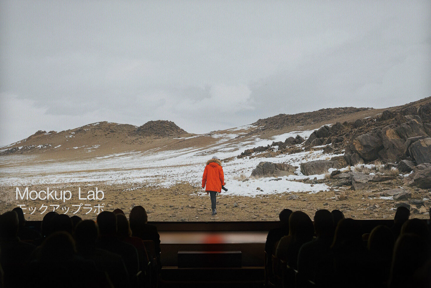 Cinema audience viewing a large screen displaying a snowy landscape with a person in an orange coat. Ideal for mockup templates and graphic design.