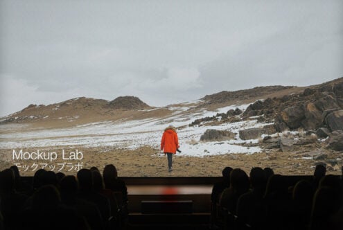 Cinema audience viewing a large screen displaying a snowy landscape with a person in an orange coat. Ideal for mockup templates and graphic design.