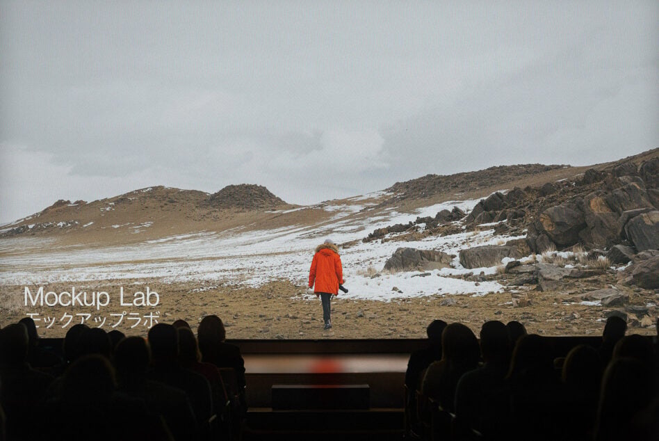 Cinema screen showing snowy mountain landscape with runner in red jacket, viewers visible