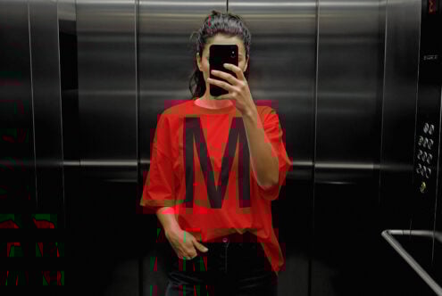 Mockup of a red T-shirt with a bold black letter M in an elevator setting. Perfect for apparel design presentations and graphic designers.