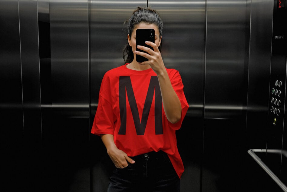 Mockup of a red T-shirt with a bold black letter M in an elevator setting. Perfect for apparel design presentations and graphic designers.