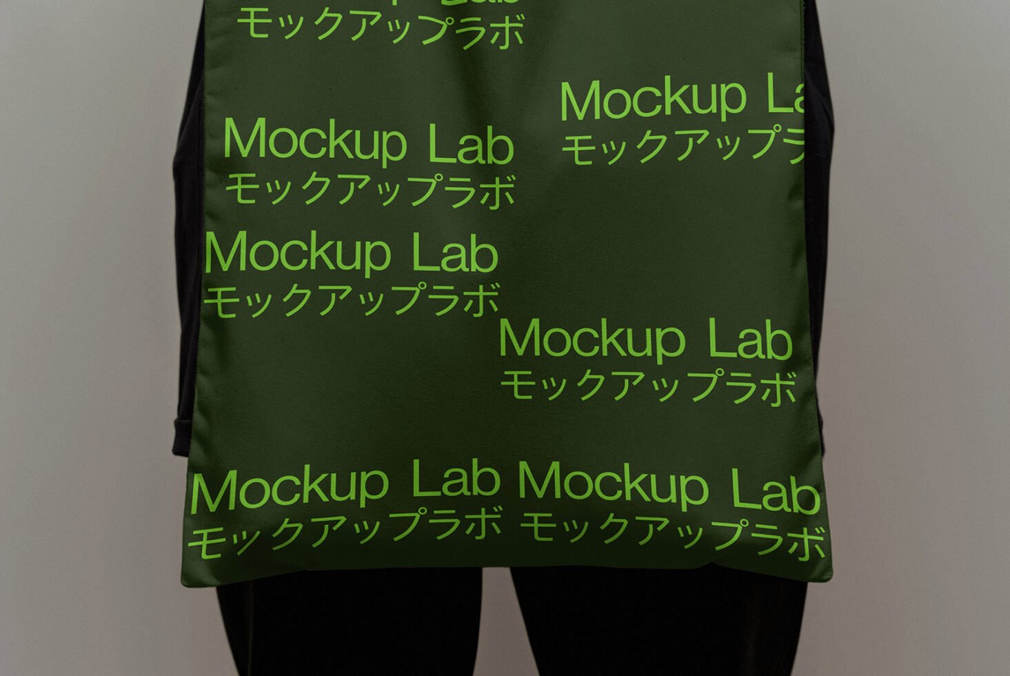 Green tote bag mockup featuring repeated text Mockup Lab with Japanese characters. Ideal for branding projects and design presentations. Mockup graphics.