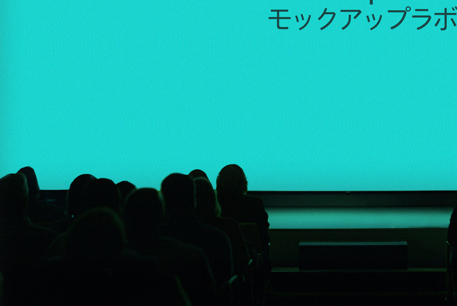 Audience watching presentation with blue screen and Japanese text. Ideal for seminar mockup design, conference graphics, and template resources for designers.