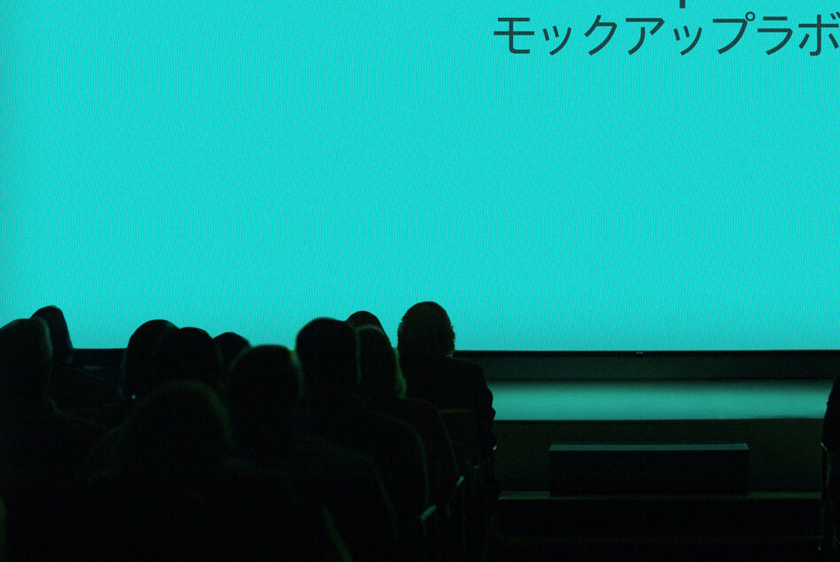 Movie theater screen with bright turquoise backdrop, audience silhouettes in foreground