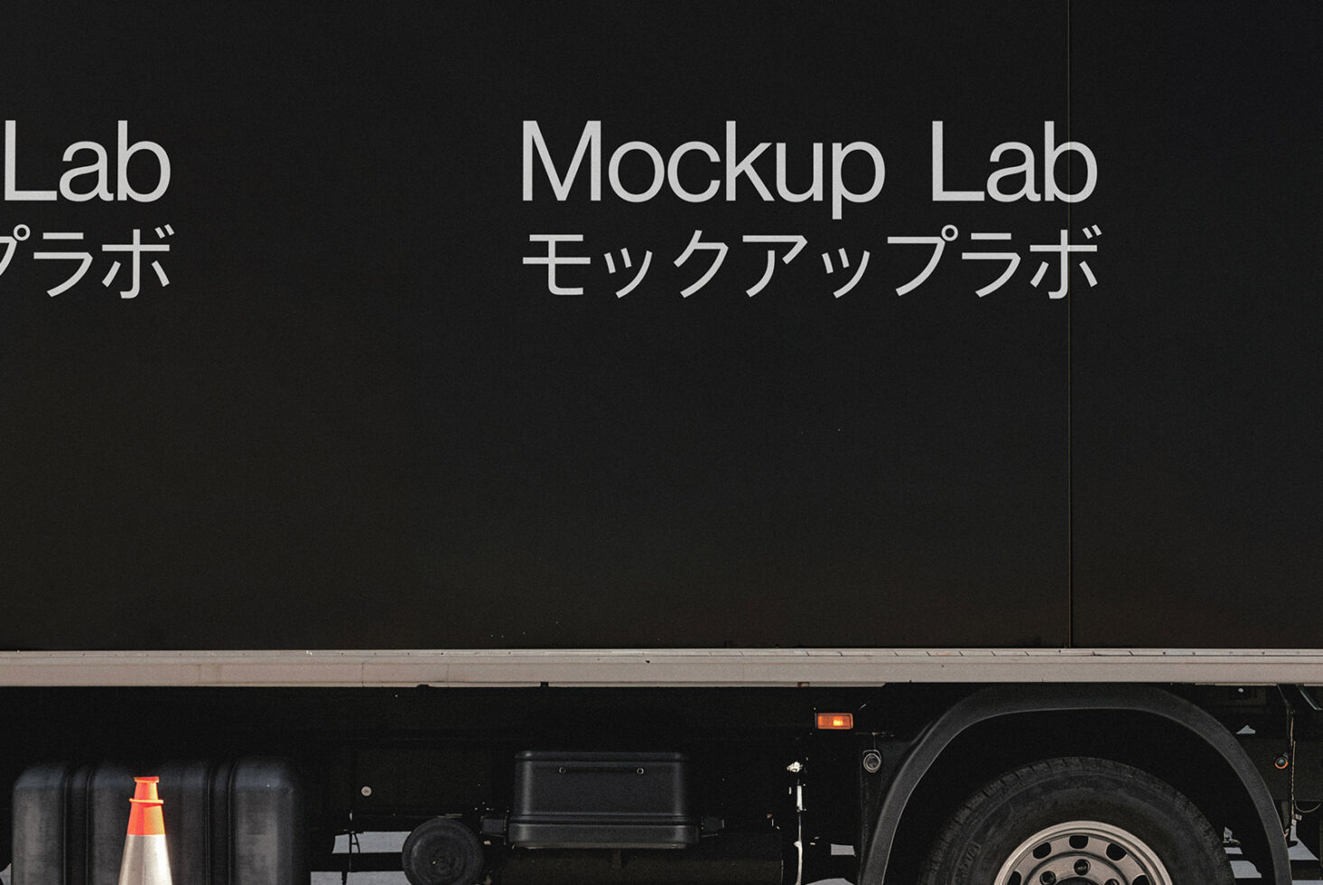 Truck with text Mockup Lab in English and Japanese on its side parked near a traffic cone. Ideal for graphic design mockups and branding templates.