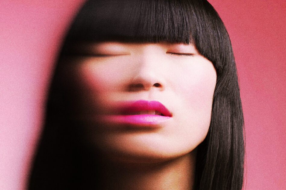 Woman with blunt bangs against pink background wearing bold magenta lipstick