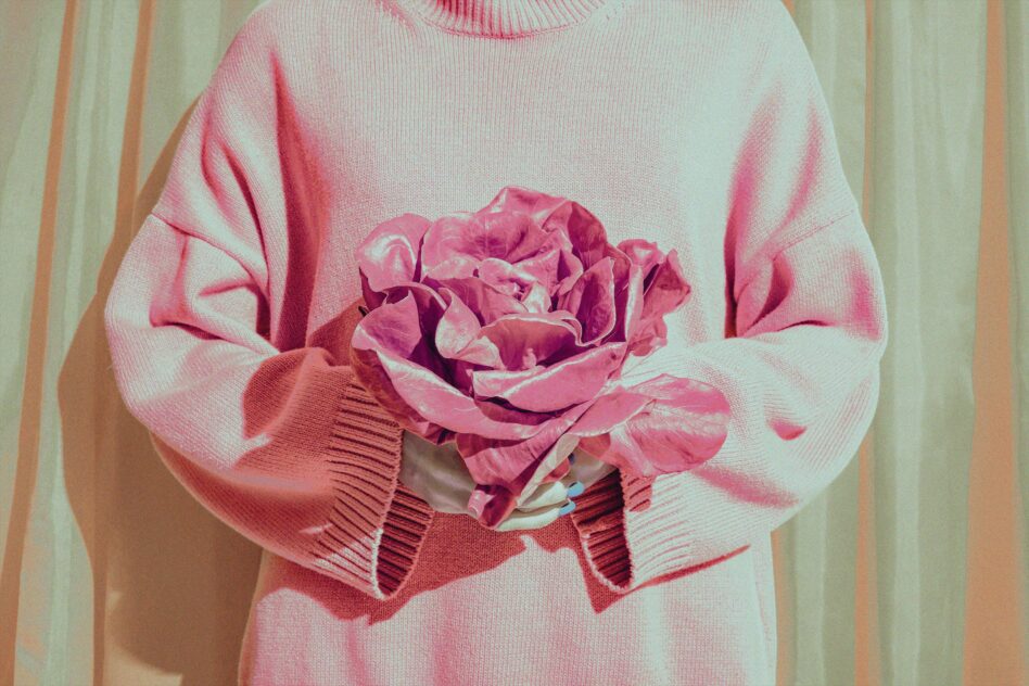 Person in pink sweater holding pink flowers, suitable for mockups and templates. Ideal for designers seeking vibrant backgrounds and unique compositions.