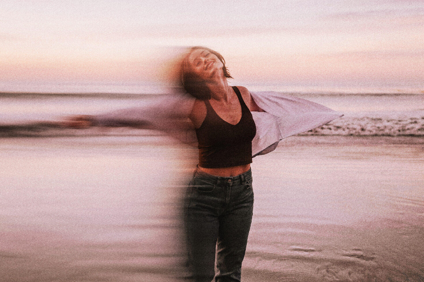 Woman in black top on beach with pink fabric flowing behind her at sunset