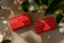 Red business card mockups lying on textured wood with blurred green plant in background