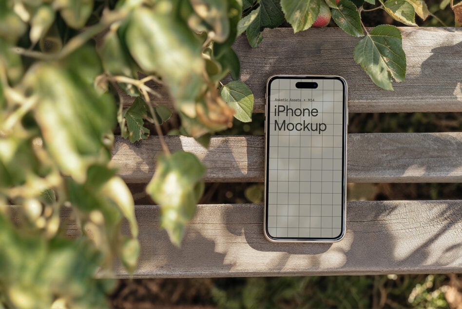Phone mockup propped on weathered wooden bench with leafy branches overhead