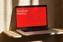MacBook mockup on wooden surface with red grid screen design. Ideal for showcasing UI templates and digital assets for designers seeking quality mockups.