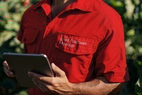 Person in red shirt holding a tablet with mockup design on the pocket. Keywords: mockup, design, template, graphic, shirt, foldover, digital assets.