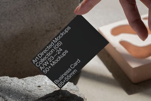 Minimal business card mockup leaning on stone with hand. Ideal for designers. Keywords: mockup, business card, design template, minimalist.
