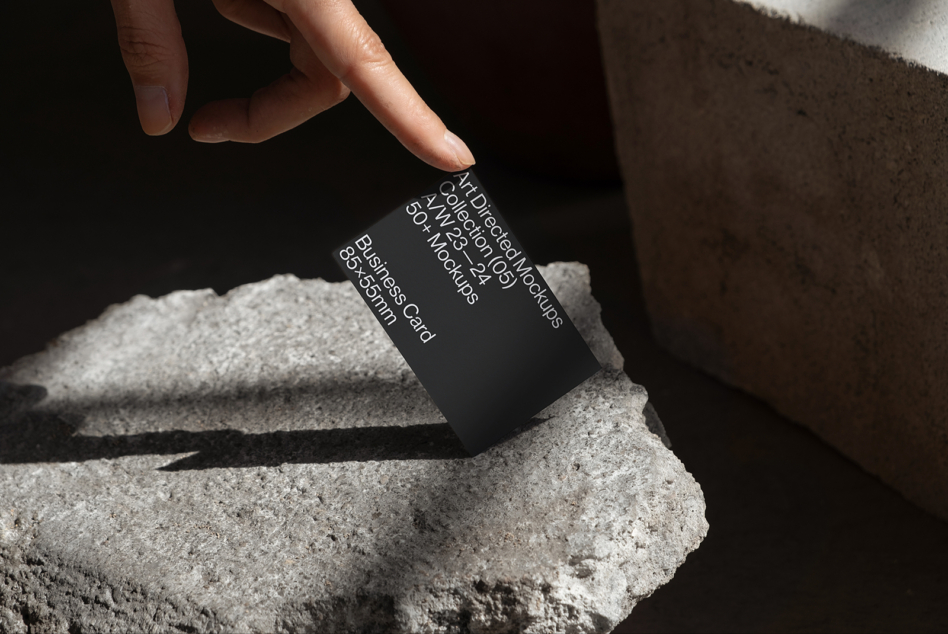 Hand holding black business card mockup on concrete edge with shadow