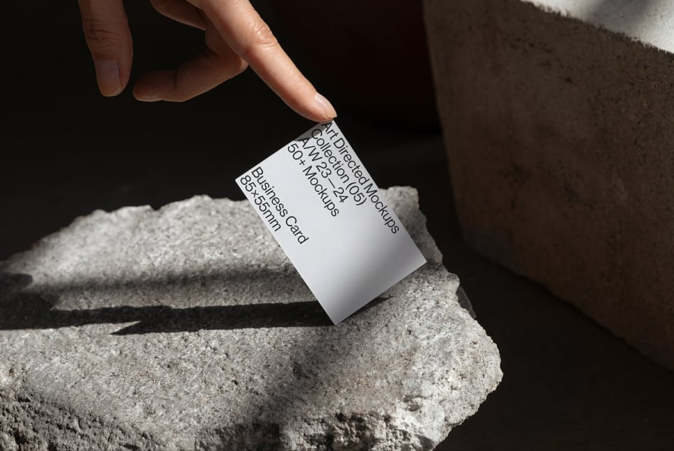 Hand holding white business card mockup against rough stone surface