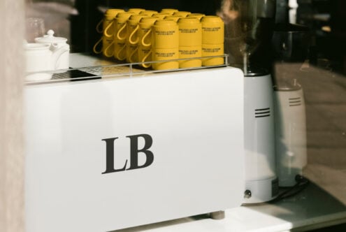 Cafe counter with white espresso machine labeled LB and lined yellow mugs. Ideal for mockup designs, coffee shop graphics, branding visuals.