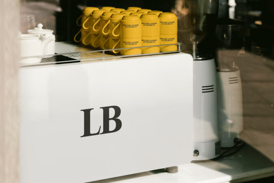 Cafe counter with white espresso machine labeled LB and lined yellow mugs. Ideal for mockup designs, coffee shop graphics, branding visuals.