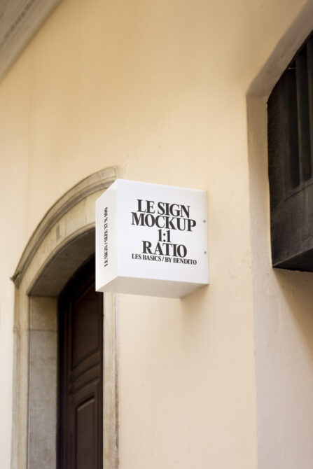 White square cube signage hanging on beige building wall by entrance