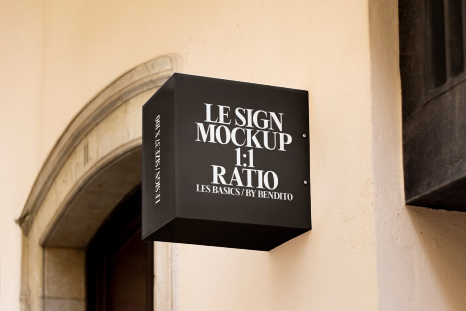 Black rectangular box sign with white typography on pale yellow building facade