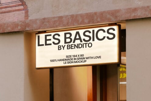Mockup of illuminated shop sign reading Les Basics by Bendito. Neutral tones on a building facade. Keywords: signage mockup, graphic design, branding.